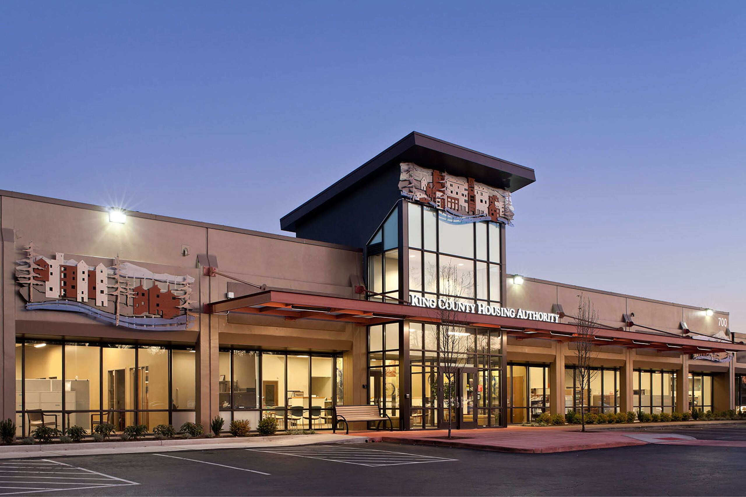 The main terminal building of King County International Airport (Boeing Field) in Seattle, WA, featuring a red brick façade, arched windows, a clock, and an American flag flying above against a clear blue sky.